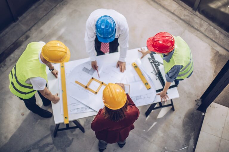 four people gathered arounf construction drawing on a table
